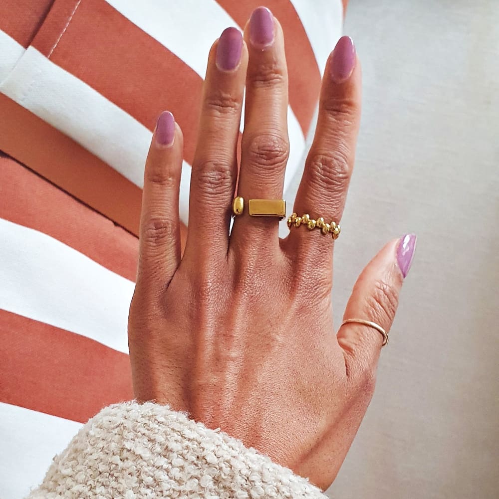 Hand with gold rings and pink nail polish against a blurred background